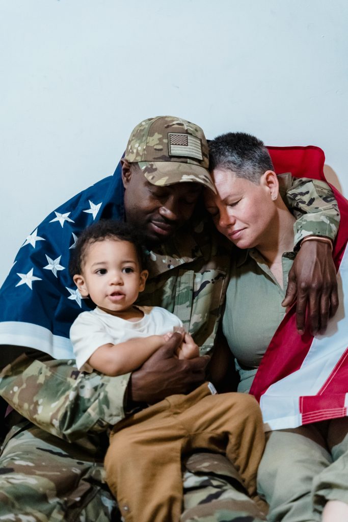 Emotional family reunion with a soldier wrapped in an American flag, embracing loved ones.
